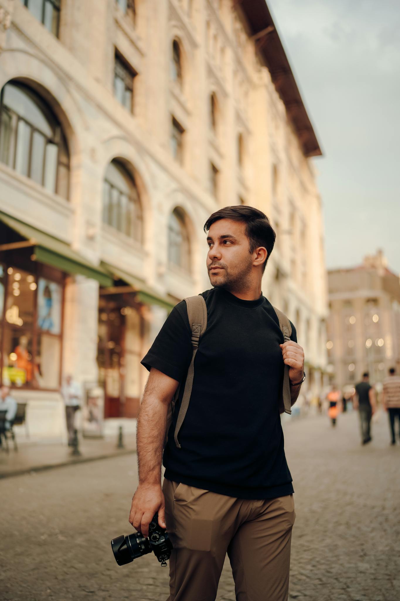 Man with camera backpack explores historic city streets at sunset.
